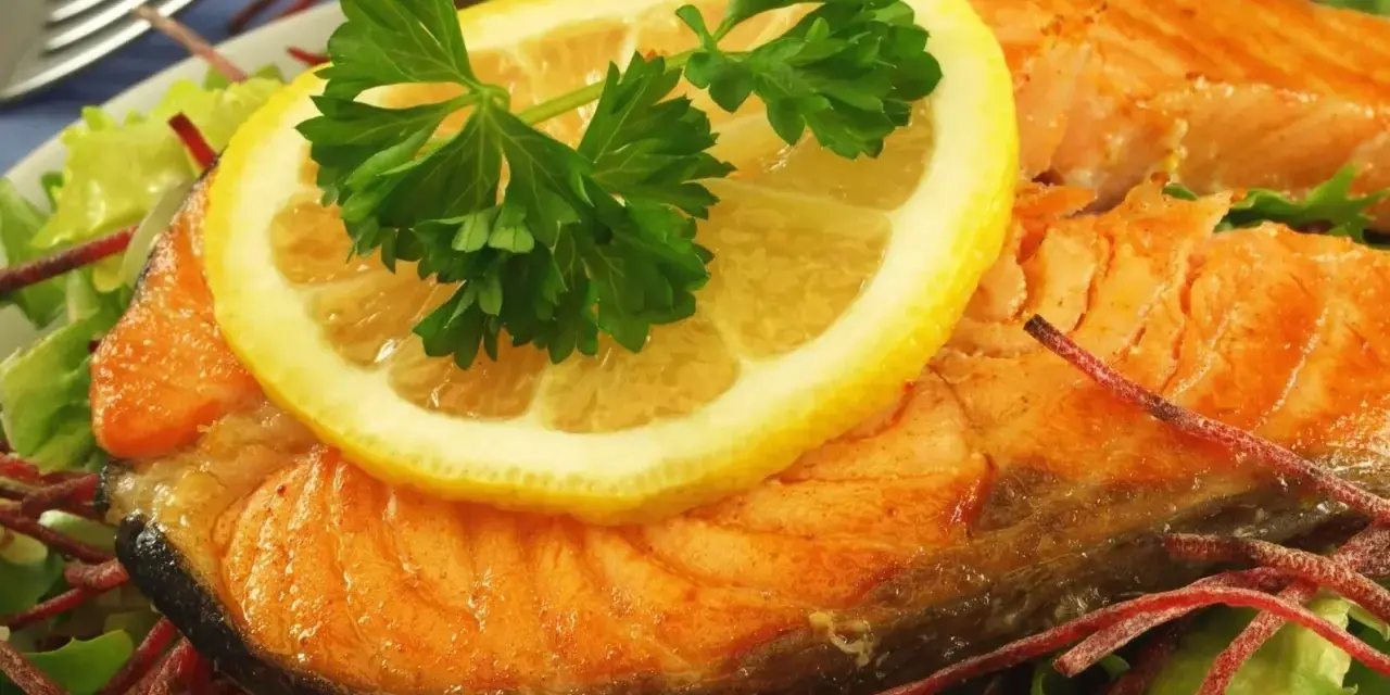 Pyszny łosoś z piekarnika, podany z plasterkiem cytryny i natką pietruszki na sałatce.