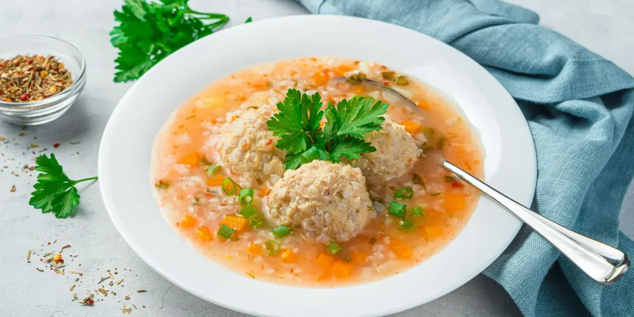 Szybka zupa na obiad z klopsikami, ryżem i warzywami, udekorowana natką pietruszki.
