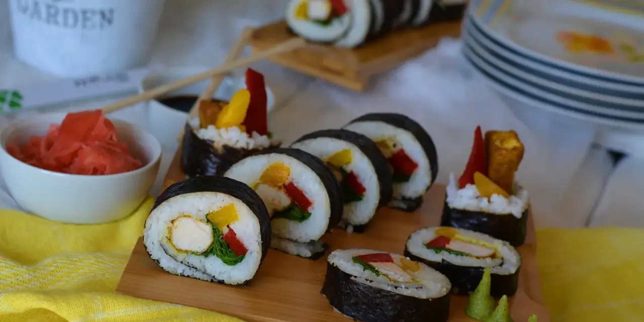 Pyszne sushi z kurczakiem, papryką i mango. Podane na desce z dodatkami: marynowanym imbirem i wasabi.