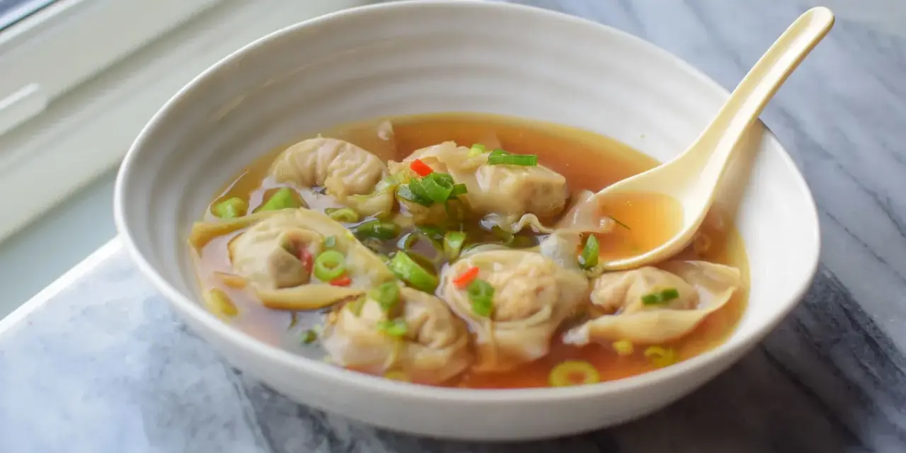 Aksamitna zupa wonton z kawałkami chili i szczypiorku, gotowa do nabrania łyżką.
