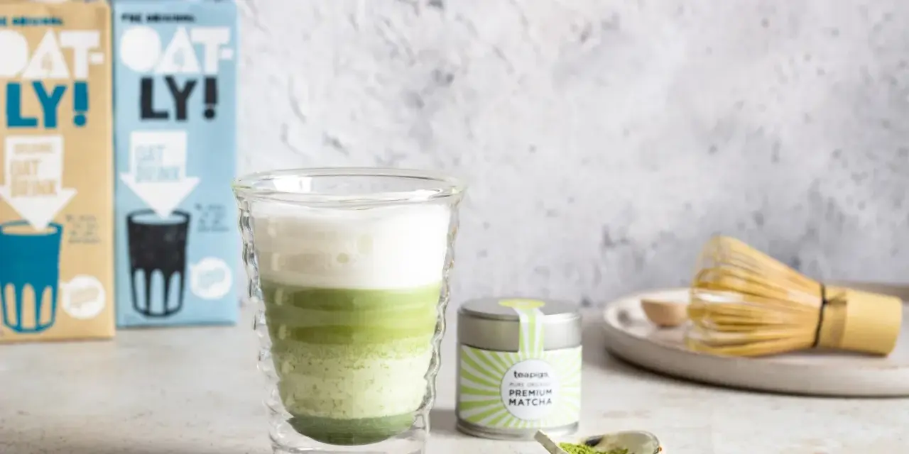 Zielony napój warstwowy w szklance, obok puszka z napisem "PREMIUM MATCHA" i bambusowa miotełka. To jest właśnie co to matcha.