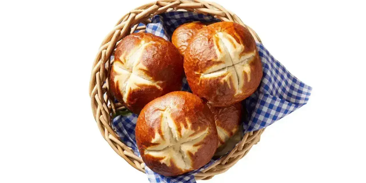 Koszyk z kilkoma bułkami bawarskimi, ułożonymi na niebiesko-białej kratkowanej ściereczce.