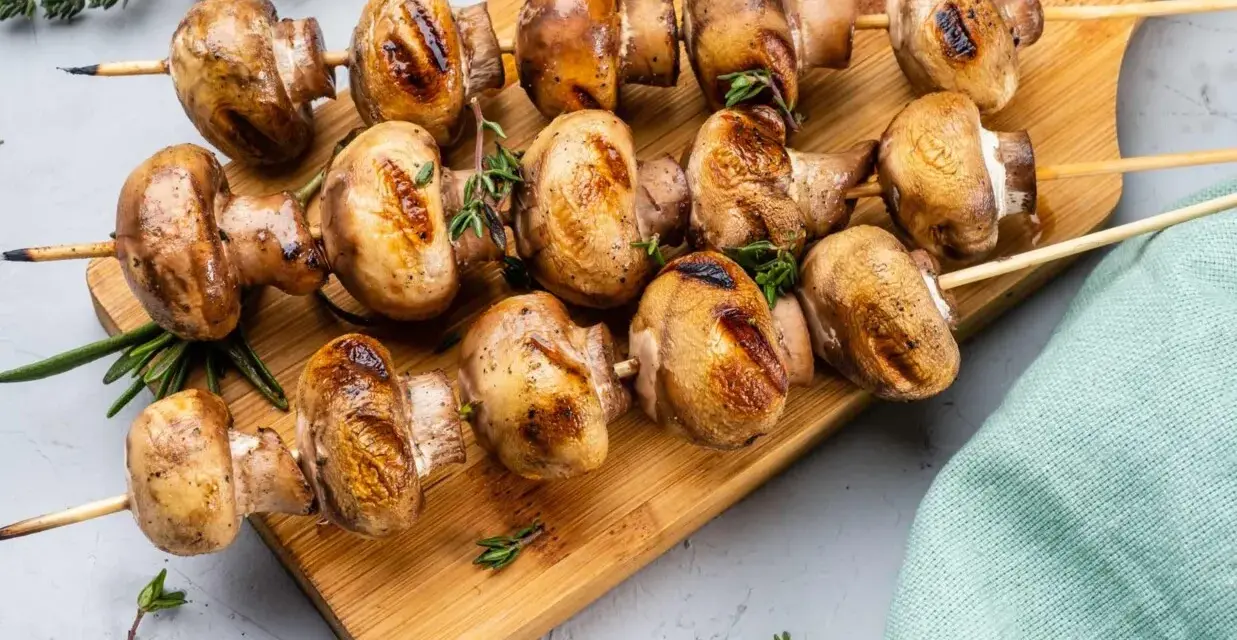 Grillowane pieczarki na drewnianej desce, przyprawione ziołami. Idealne na letnie przyjęcie.
