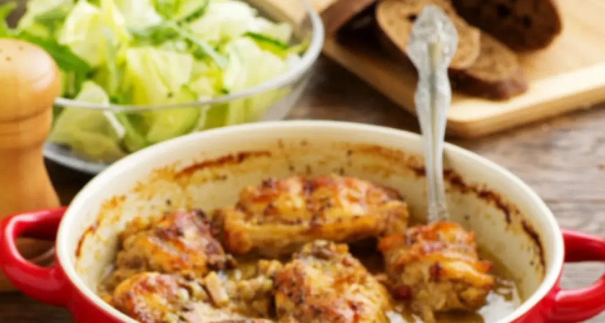 Pieczony królik w czerwonej naczyniu, z dodatkiem marynaty do królika pieczonego w piekarniku, podany z sałatką i chlebem.