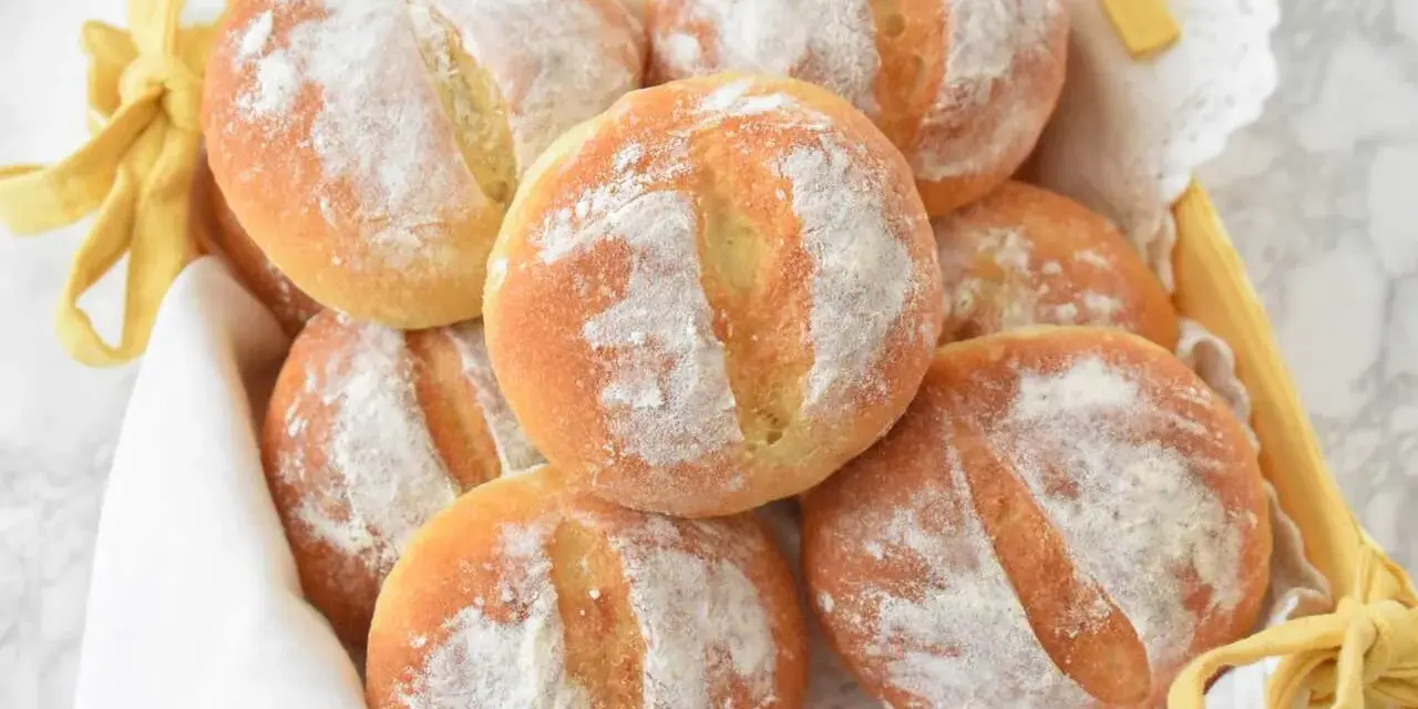 Koszyk pełen świeżych, puszystych bułek ziemniaczanych, posypanych mąką. Idealne na śniadanie.