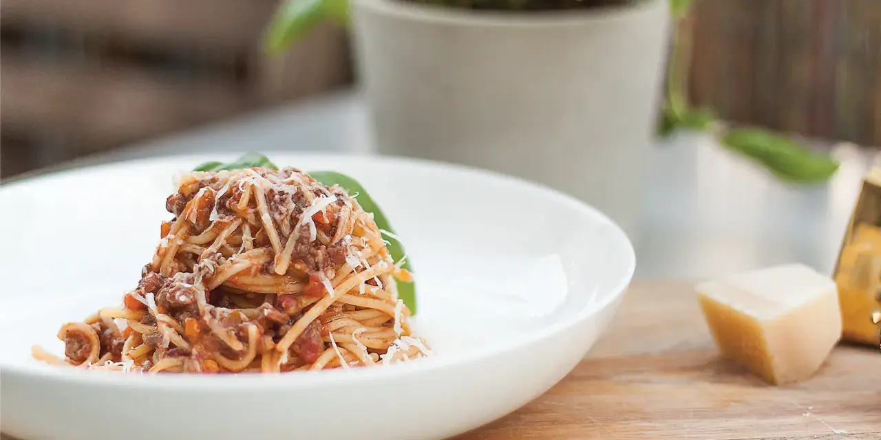 Pyszne spaghetti bolognese, przygotowane według oryginalnego przepisu, posypane parmezanem i udekorowane listkiem bazylii.