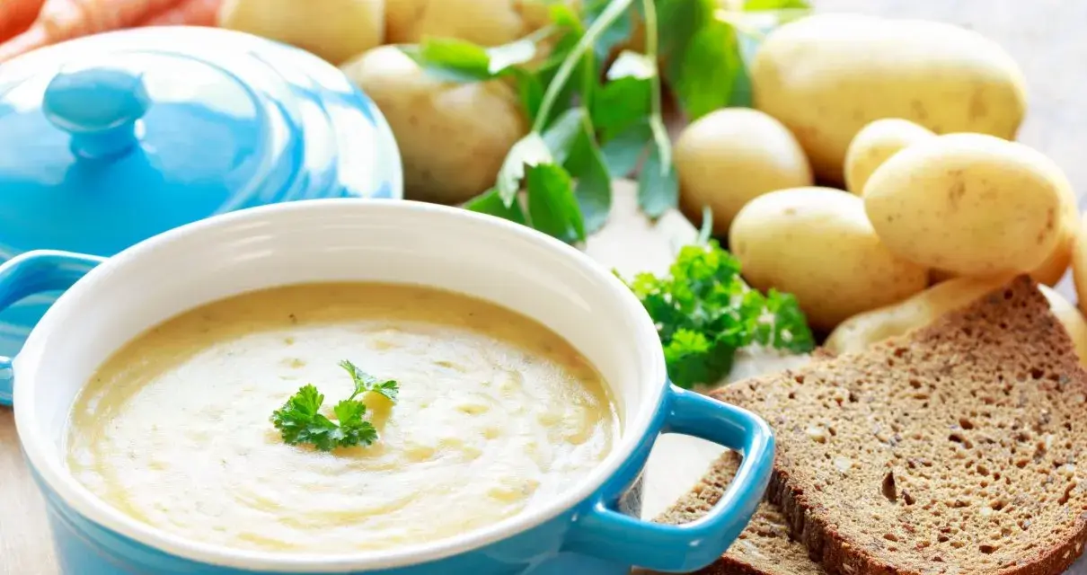 Aksamitna zupa ziemniaczana, przepis babci, z chlebem i świeżymi ziemniakami w tle.