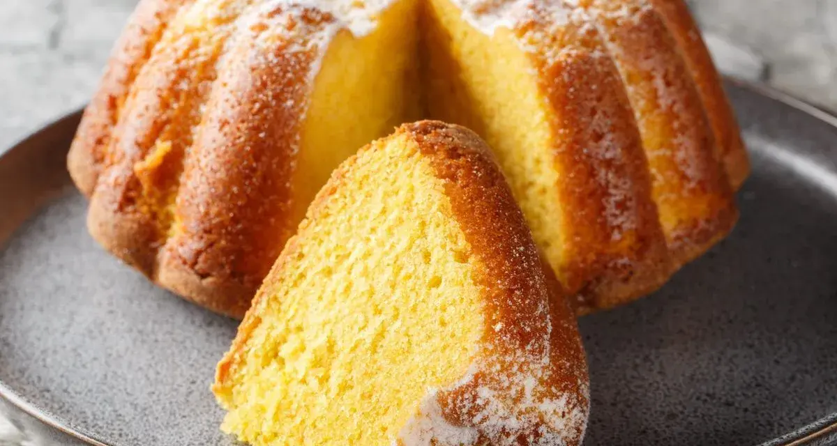 Puszysta babka na maślance, oprószona cukrem pudrem, z wyciętym kawałkiem na talerzu.