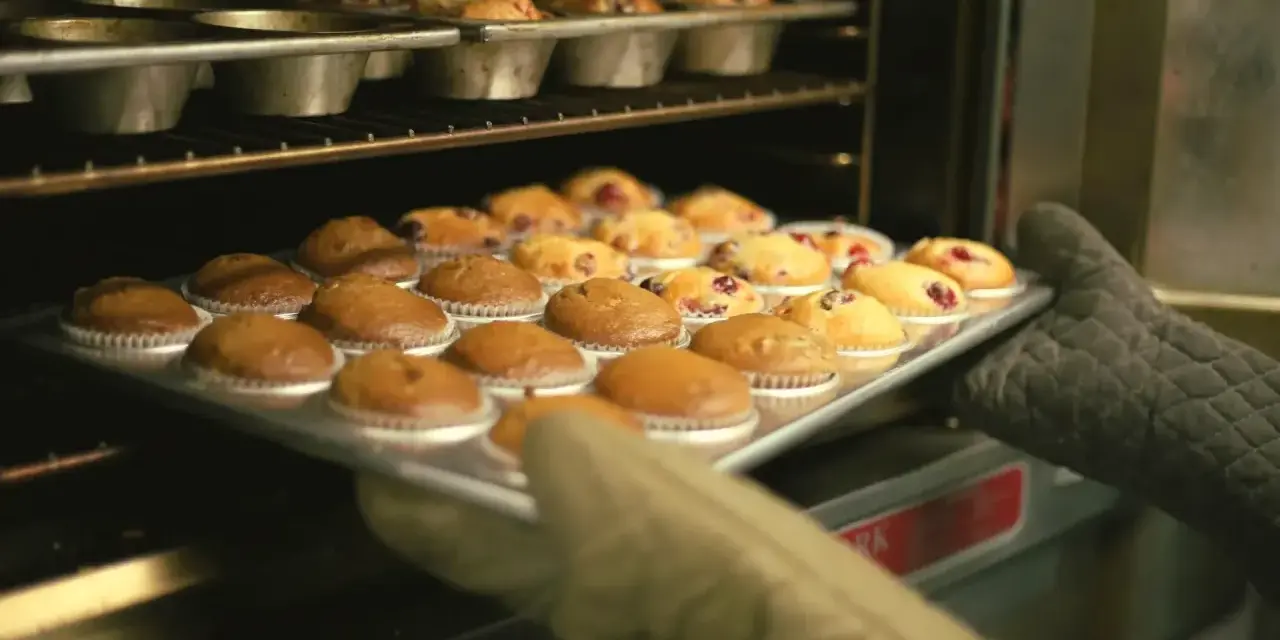 Rękawice wyjmują z piekarnika blachę z gotowymi muffinkami, które idealnie nadają się do przepisu na wilgotne i puszyste muffinki.
