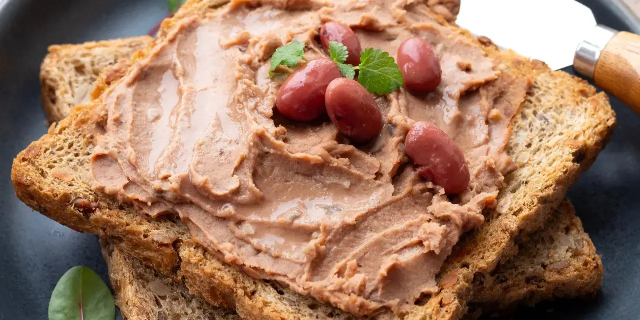 Pyszna pasta z czerwonej fasoli na chrupiących tostach pełnoziarnistych, udekorowana fasolkami i listkami ziół.