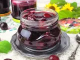 Słoiczek pełen wiśniowej frużeliny, obok świeże wiśnie i listki mięty.