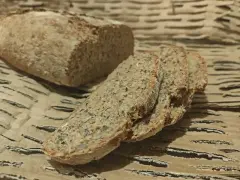 Chleb orkiszowy przepis: świeżo upieczony bochenek i kromki z ziarnami na brązowym tle.