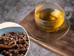 Napar z goździków przepis: aromatyczna herbata w szklance i miseczka pełna goździków na drewnianej desce.
