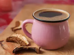 Różowy kubek z aromatyczną kawą grzybową na drewnianej desce, obok suszone grzyby.