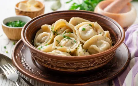Pielmieni co to? Aromatyczne, gorące pierożki w glinianej misie, posypane zieloną natką. Obok miseczki z masłem i posiekanym szczypiorkiem.