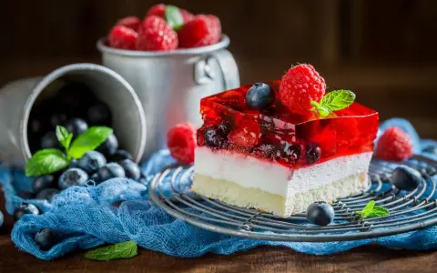 Pyszna galaretka z owocami, malinami i borówkami, na biszkoptowym spodzie, ozdobiona listkiem mięty.