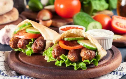 Dwa pyszne **ćevapi** w bułce z sałatą, pomidorem i ogórkiem, podane z sosem.