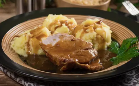Karkówka w sosie własnym z purée ziemniaczanym, udekorowana natką pietruszki. Pyszny sos do karkówki idealnie komponuje się z ziemniakami.