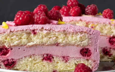 Pyszny tort z warstwami biszkoptu, przełożony kremem malinowym z mascarpone i świeżymi malinami.