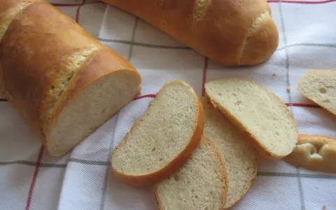 Chrupiąca bułka wrocławska, pokrojona w kromki, leży obok całej bagietki na lnianym obrusie.