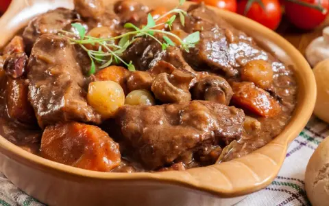 Gęsta, aromatyczna łata wołowa z warzywami i grzybami, podana w glinianej misie, udekorowana gałązką ziół.