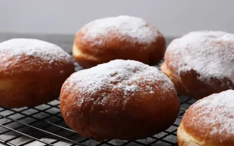 Szybkie pączki z piekarnika, oprószone cukrem pudrem, wyglądają apetycznie na czarnej kratce.
