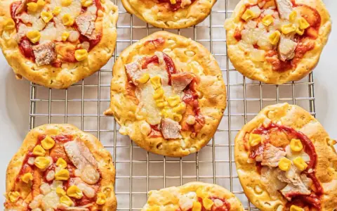 Mini pizze z serka wiejskiego, z kukurydzą i kawałkami mięsa, ułożone na metalowej kratce.
