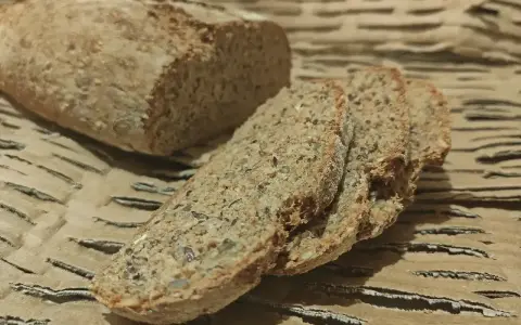 Chleb orkiszowy przepis: świeżo upieczony bochenek i kromki z ziarnami na brązowym tle.