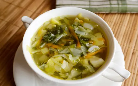 Aromaticzna zupa z młodej kapusty z ziemniakami i marchewką, podana w białej miseczce na bambusowej macie.
