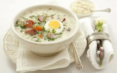 Aromaticzny żurek z białą kiełbasą i jajkiem, podany w misce, z dodatkiem ziół i marchewki. Idealny prosty przepis na żurek.