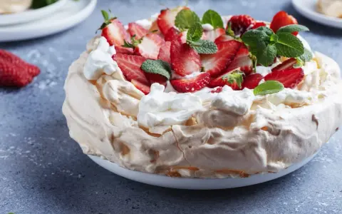Puszysty tort bezowy z mascarpone i bitą śmietaną, ozdobiony świeżymi truskawkami i miętą.