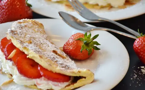 Słodki omlet z truskawkami i bitą śmietaną, posypany cukrem pudrem. Idealny przepis na omlet na słodko.