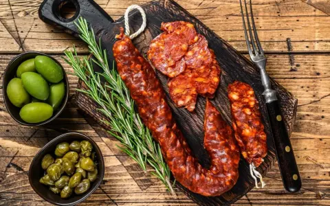 Chorizo co to? Pikantna, wędzona kiełbasa na desce z oliwkami, kaparami i rozmarynem. Idealna przekąska.