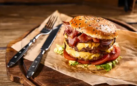 Podwójny burger z soczystym mięsem na burgery, serem, bekonem i warzywami, gotowy do zjedzenia z widelcem i nożem.
