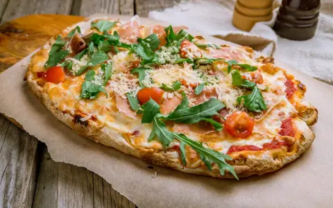 Pinsa co to? Podłużna, chrupiąca pizza z rukolą, pomidorkami i szynką parmeńską, posypana parmezanem.