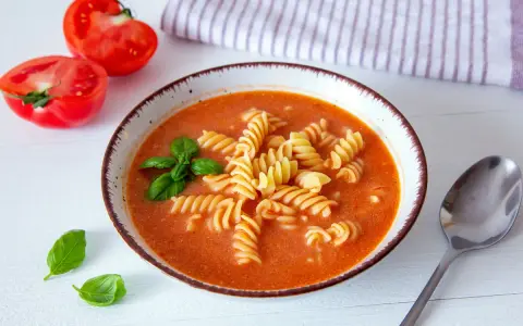 Aksamitna zupa pomidorowa z makaronem fusilli, ozdobiona bazylią. Idealne jakie przyprawy do zupy pomidorowej? Świeże pomidory obok sugerują prostotę i smak.