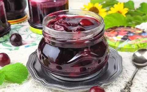 Słoiczek pełen wiśniowej frużeliny, obok świeże wiśnie i listki mięty.