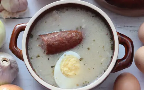 Aromaticzny żurek z kiełbasą i jajkiem, przygotowany na bazie domowego zakwasu na żurek. Obok czosnek, cebula i jajka.