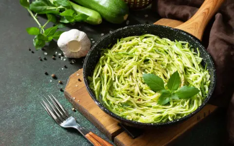 Pyszny makaron keto z cukinii w patelni, udekorowany bazylią. Obok czosnek, pieprz i świeże cukinie.