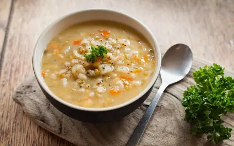 A miseczka parującego krupniku, pachnącego jak zupa krupnik przepis babci. Obok łyżka i gałązka natki pietruszki.