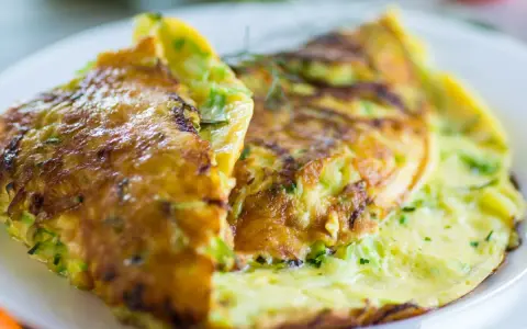 Złocisty omlet z cukinią, delikatnie zrumieniony, podany na białym talerzu.
