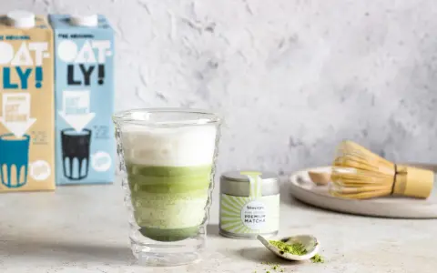 Zielony napój warstwowy w szklance, obok puszka z napisem "PREMIUM MATCHA" i bambusowa miotełka. To jest właśnie co to matcha.