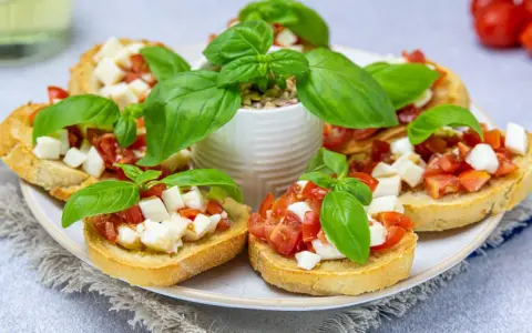 Bruschetta z pomidorami i mozzarellą, świeża bazylia i chrupiące pieczywo. Idealny przepis na letnią przekąskę.
