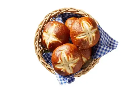 Koszyk z kilkoma bułkami bawarskimi, ułożonymi na niebiesko-białej kratkowanej ściereczce.