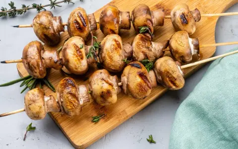Grillowane pieczarki na drewnianej desce, przyprawione ziołami. Idealne na letnie przyjęcie.