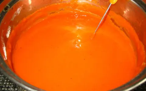 Gęsty, pomarańczowy sos do gołąbków w garnku, z widoczną sondą termometru.