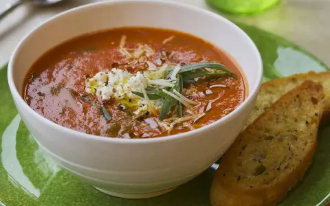 Aksamitna zupa solferino z serem feta i grzankami czosnkowymi na zielonym talerzu.
