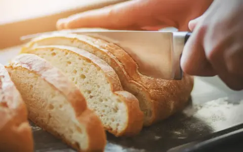 Dłoń kroi świeży chleb na kromki. Zastanawiasz się, jak odświeżyć chleb? Ten obrazek pokazuje, jak zacząć.