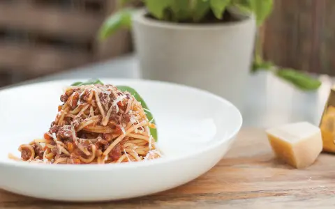 Pyszne spaghetti bolognese, przygotowane według oryginalnego przepisu, posypane parmezanem i udekorowane listkiem bazylii.
