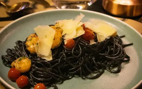 Czarny makaron z krewetkami, pomidorkami koktajlowymi i płatkami parmezanu na talerzu.